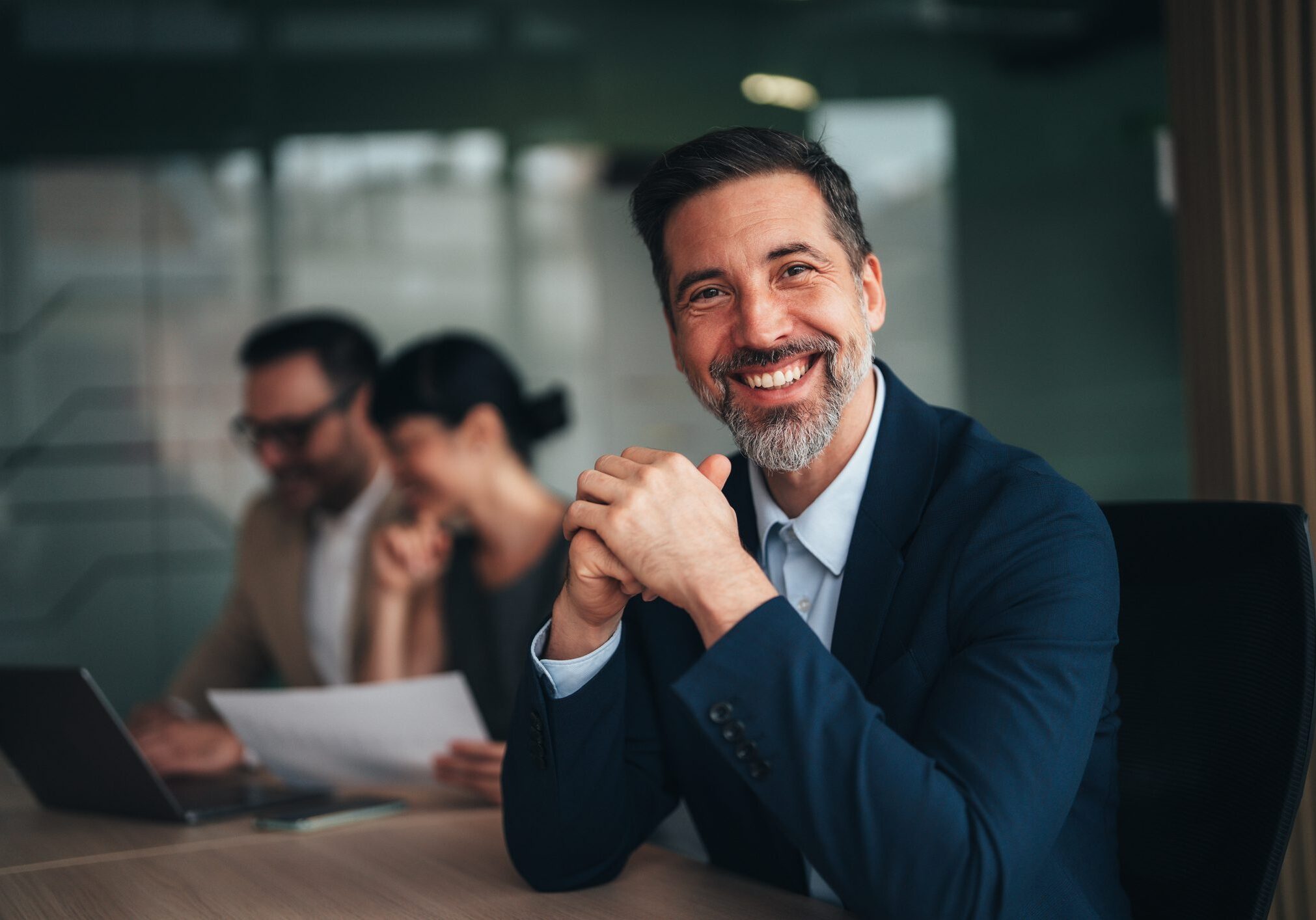 Portrait of handsome smiling businessman with his colleagues. Multi-ethnic group of business persons in modern office. Successful team leader and his team in background.
